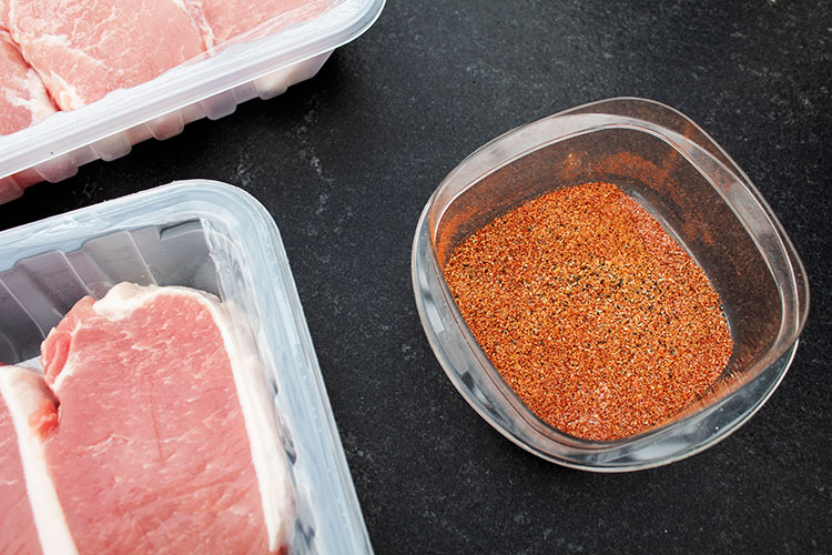 overhead view of raw sliced pork chops in package and pork chop rub mixed in bowl next to the right