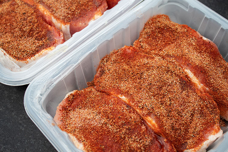 sideview of seasoned pork chops in tubs after olive oil and pork chop rub smothered on, ready to be put onto grill