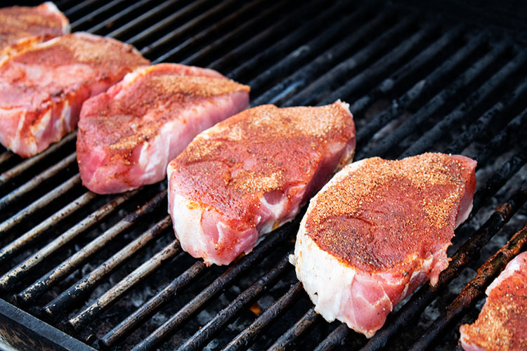 sideview of six seasoned pork chops lined up evenly on the grill