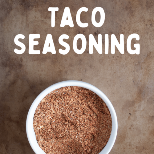 overhead view of bowl of homemade taco seasoning mixed in a small white bowl on a brown colored background