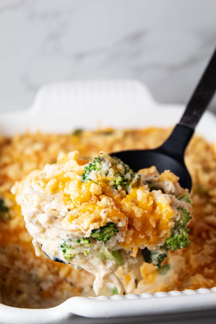 sideview of chicken cauliflower rice casserole in a white casserole dish with black serving spoon scooping one portion