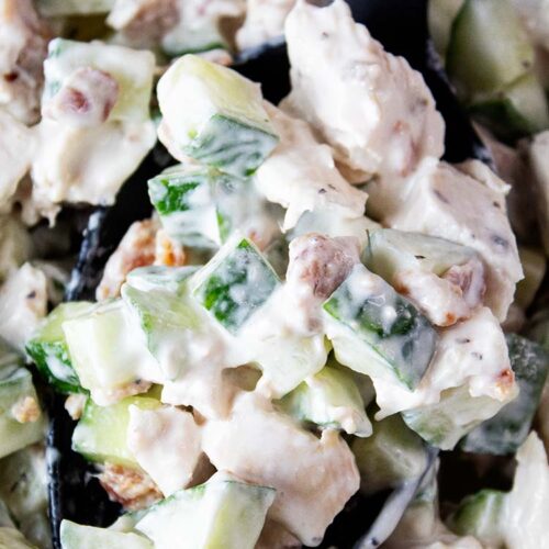 overhead view of cucumber chicken salad with large black serving spoon scooping a serving from the bowl