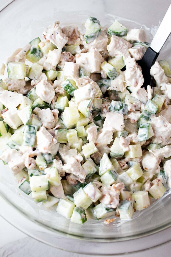 overhead view of thoroughly combined cucumber chicken salad in a glass mixing bowl with a serving spoon