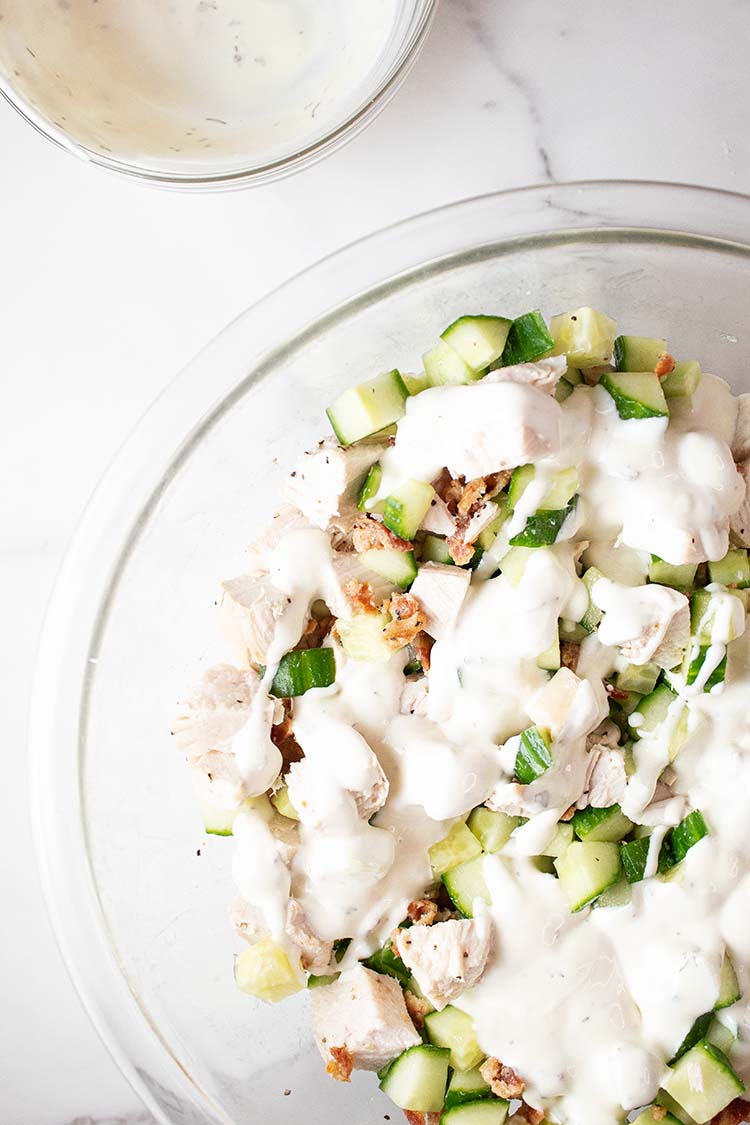 overhead view of combined ingredients in glass mixing bowl with dressing poured over waiting to be thoroughly mixed