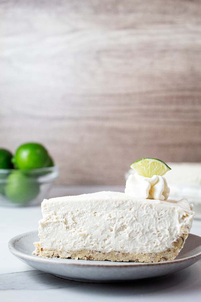 sideview of slice of no bake key lime cheesecake on a serving dish topped with key lime wedge and whipped cream
