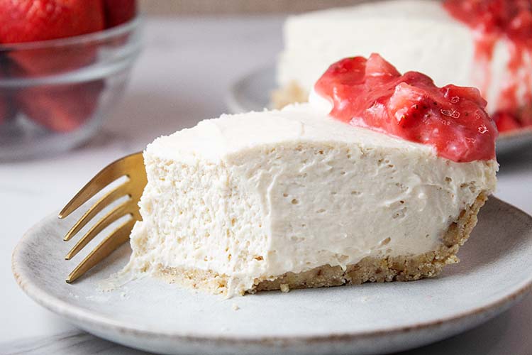 sideview of slice of rhubarb strawberry no bake cheesecake on a white serving dish with one piece removed and a gold fork laying on the plate