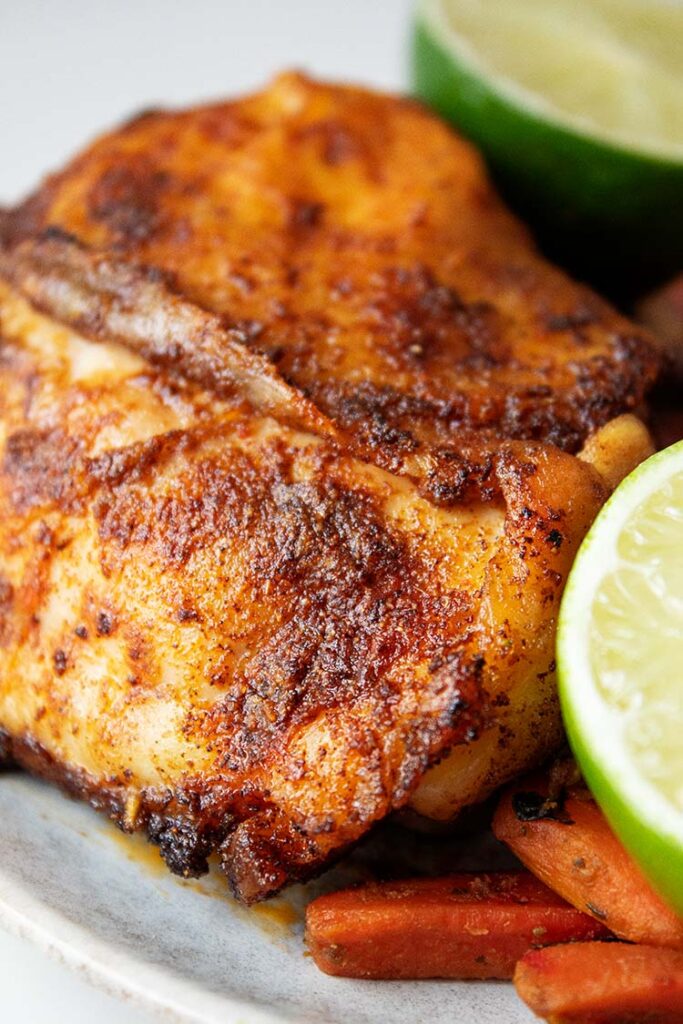 sideview of chicken chili lime after cooked in the air fryer ready to serve on white plate with two lime halves on the side