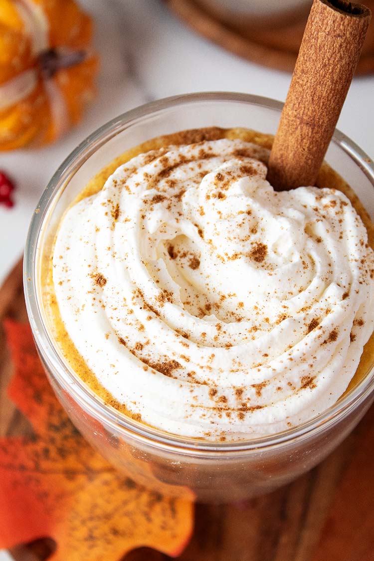 overhead view of pumpkin spice latte in a glass topped with whipped cream and vanilla stick and surrounded by fall decor