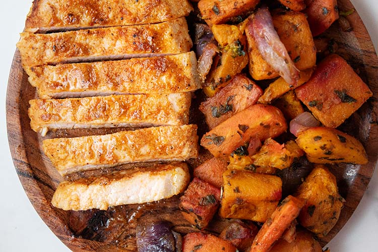 overhead view of read to serve air fryer pork chop with side of sweet potatoes on a wooden dish