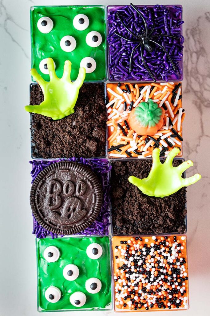 overhead view of eight ready to serve halloween cheesecake cups that are topped with eyeballs, spiders, zombies, pumpkins, and oreos