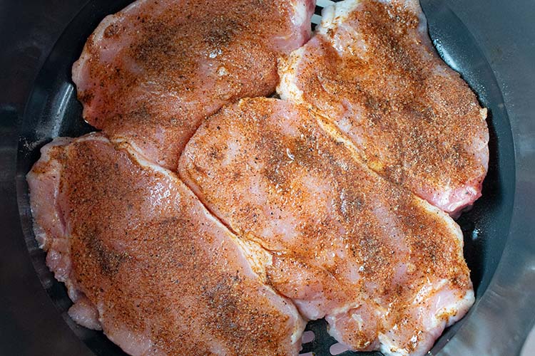 overhead view of pork chops in air fryer basket seasoned and ready to be fried