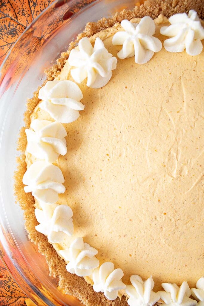 overhead view of finished no bake pumpkin cheesecake topped with whipped cream around the edges in a glass pie dish