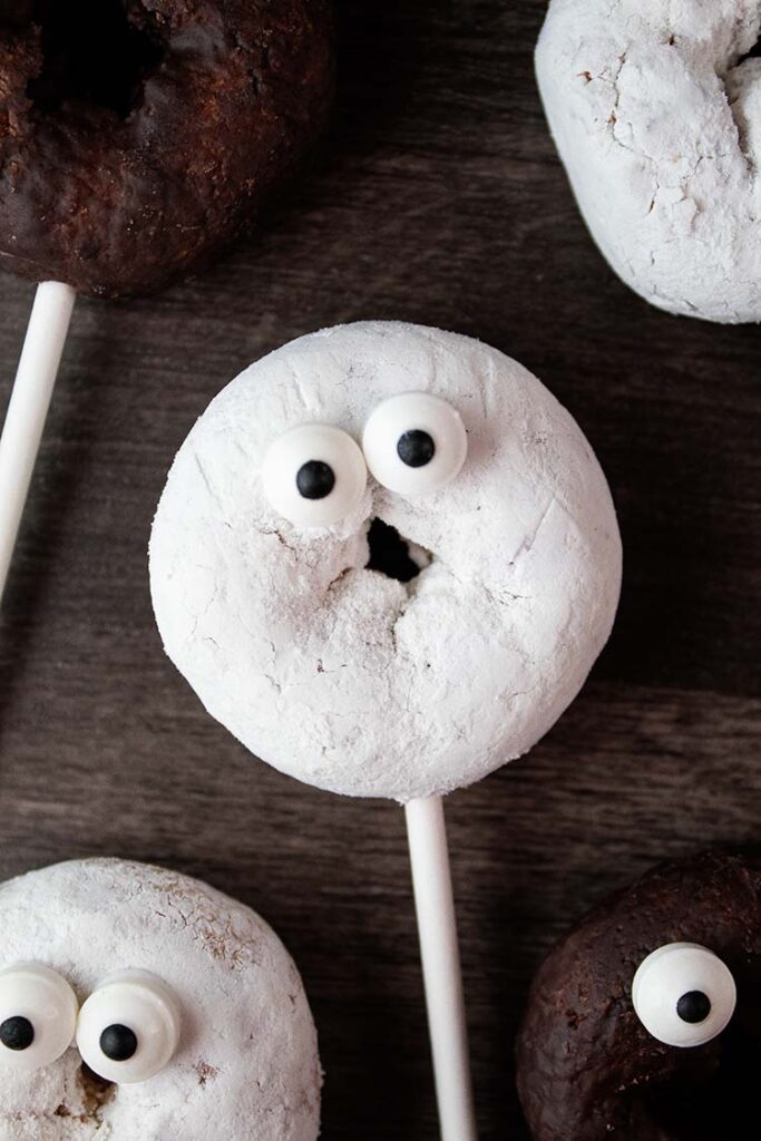 overhead view of powdered sugar and chocolate cute mini Halloween spooky donuts decorated with eyes on cake pop sticks ready to serve