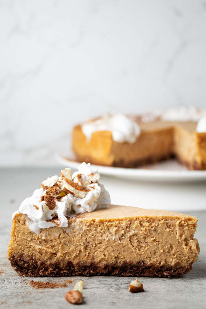 sideview of a slice of pumpkin cheesecake topped with whipped cream and cinnamon ready to serve