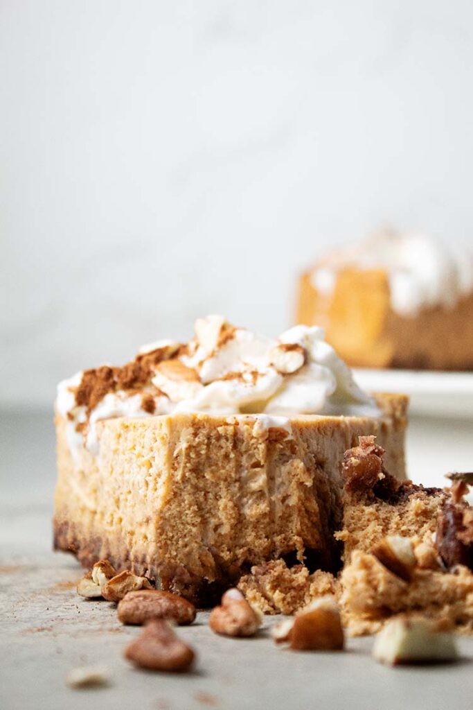 sideview of slice of pumpkin cheesecake topped with whipped cream and pecans ready to serve