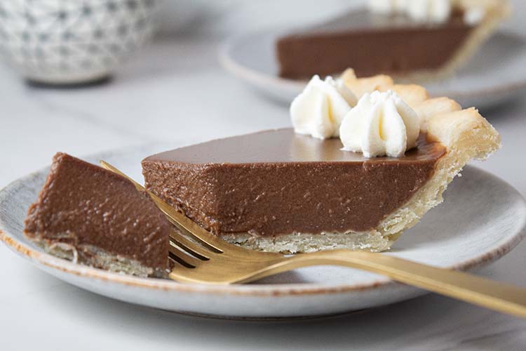 sideview of slice of chocolate pie topped with whipped cream on a serving dish and a gold fork