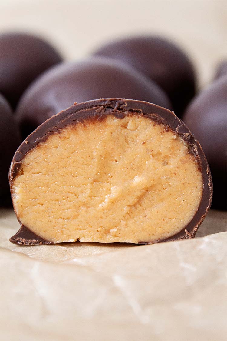 sideview of peanut butter balls on parchment paper with one sliced in half revealing the creamy peanut butter interior, all ready to be served