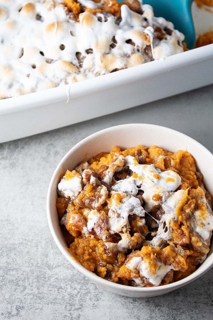 overhead view of bowl of sweet potato casserole topped with marshmallows ready to serve next to white casserole dish