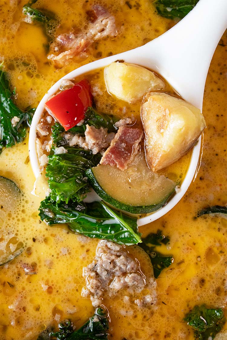 overhead view of zuppa toscana soup in a large ceramic pot with a soup ladel