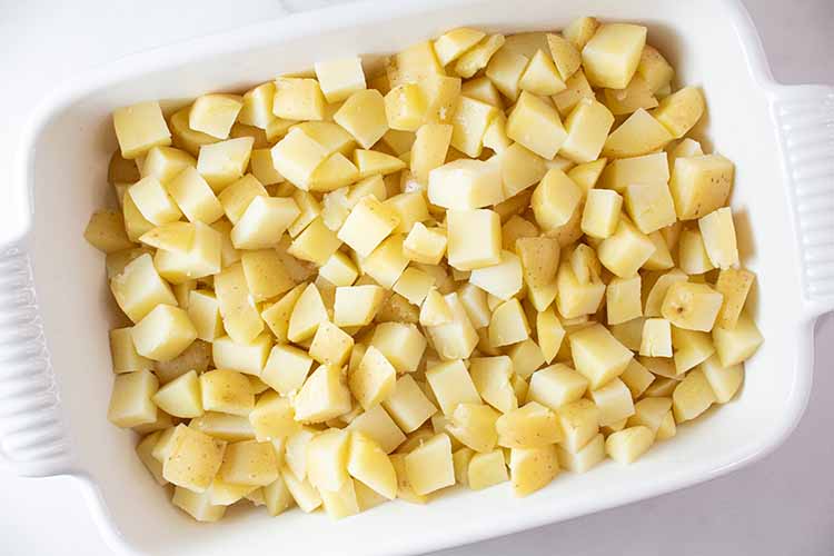 overhead view of chopped potatoes poured into white casserole dish