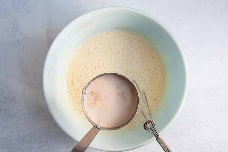 overhead view of ladel adding hot milk mixture to egg mixture to bring up temperature of egg mixture before fully combining