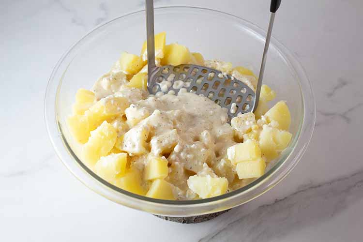 sideview of potato masher combining the potatoes with the cream mixture and mashing them