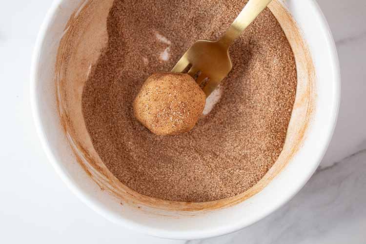 overhead view of rolled cookie ball coated with cinnamon and sugar mixture ready to be placed on a baking sheet with a fork