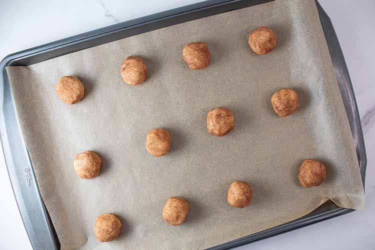 overhead view of snickerdoodle cookie balls evenly spaced 2-inches apart on a baking sheet ready to be placed into the oven