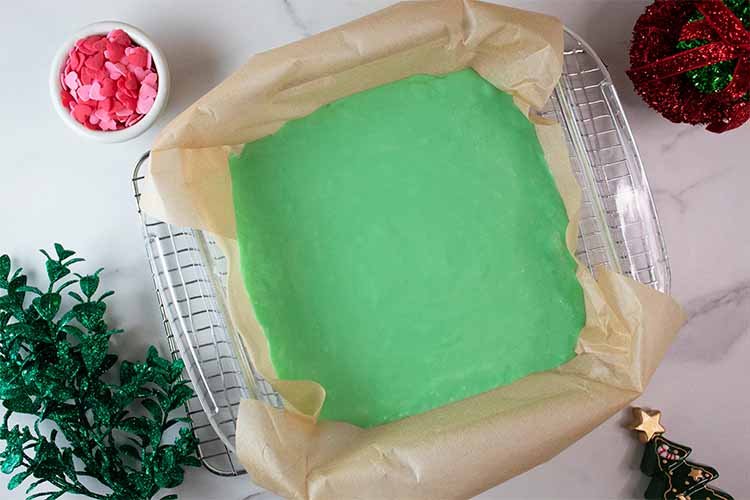 overhead view of 8-by-8 casserole dish lined with parchment paper and green fudge mixture poured in and leveled off, ready to be cooled to set