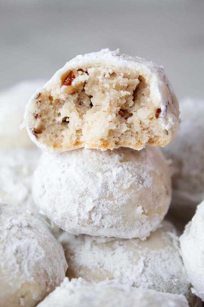 sideview of snowball cookies with pecans stacked with one cut in half and ready to serve