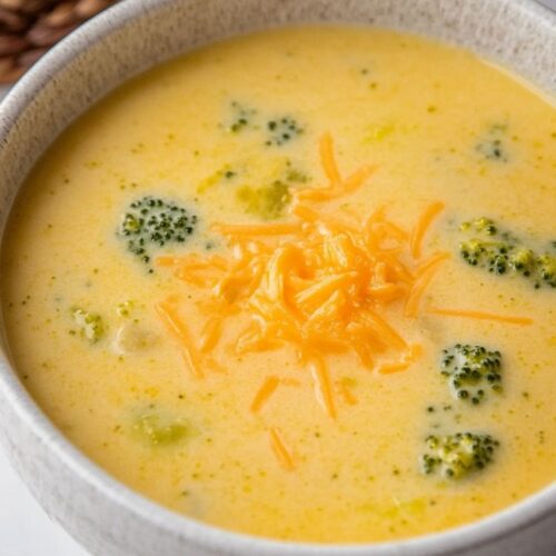 overhead view of broccoli cheddar soup in a white serving bowl and silver spoon ready to serve