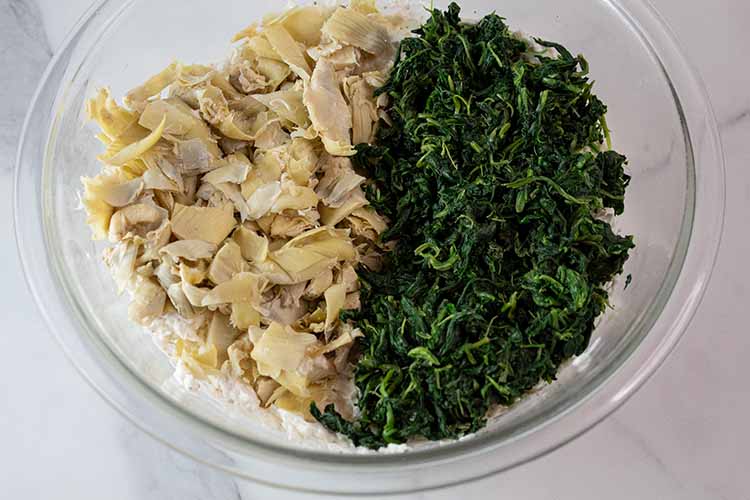 overhead view of artichokes and spinach added to the mixing bowl and read to be combined