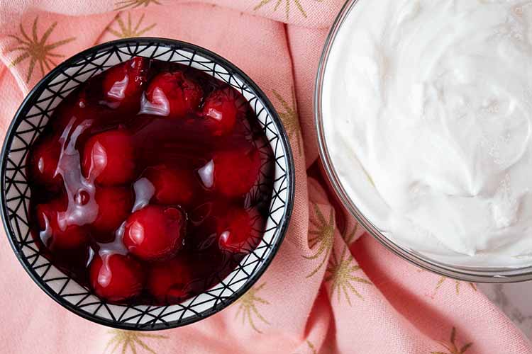 overhead view of cherry filling toppingin a bowl next to cheesecake fluff and ready to be added to it