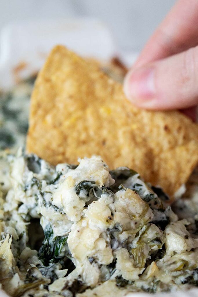 overhead view of person dipping a chip into spinach artichoke dip