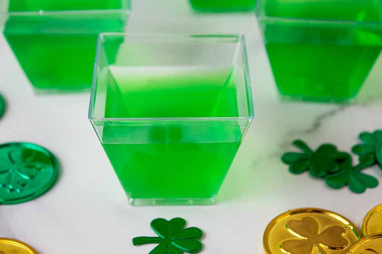 sideview of lime green jello shots in plastic cups out of the fridge and jiggly