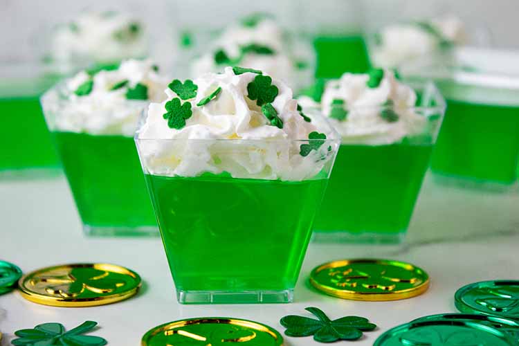 sideview of St. patrick's Day jello shots topped with sprinkles and whipped cream and decor around them