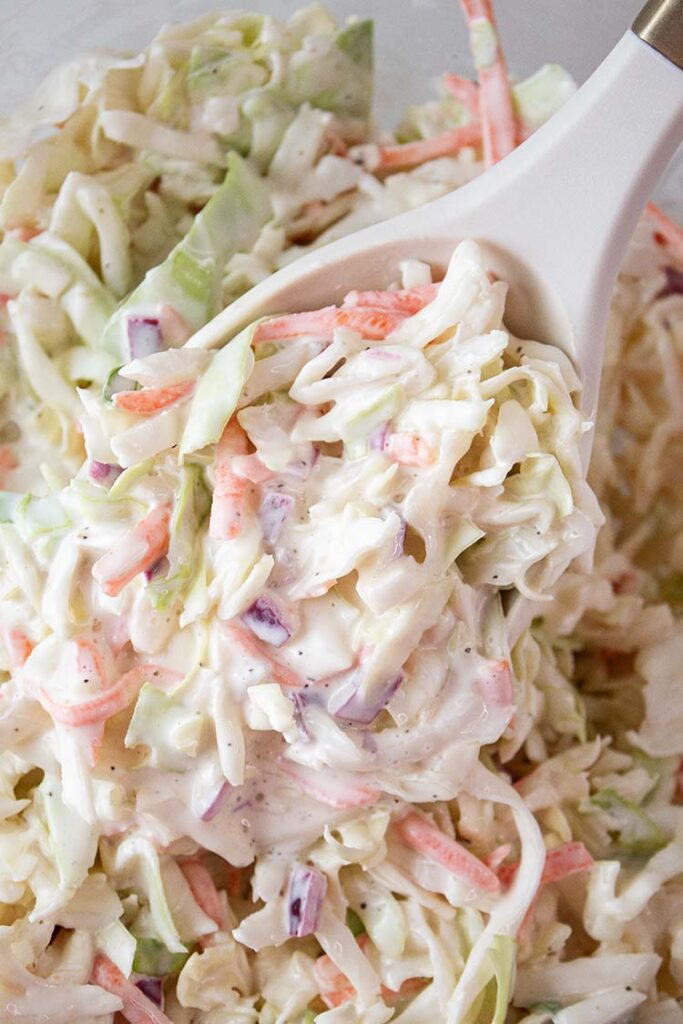 overhead view of coleslaw ready to serve with a large serving spoon removing one serving