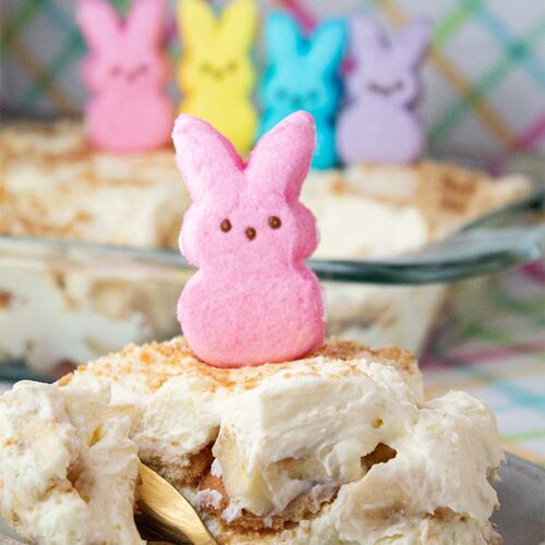 sideview of Easter banana pudding on a serving dish and casserole dish in background and both are topped with Easter Peeps decor