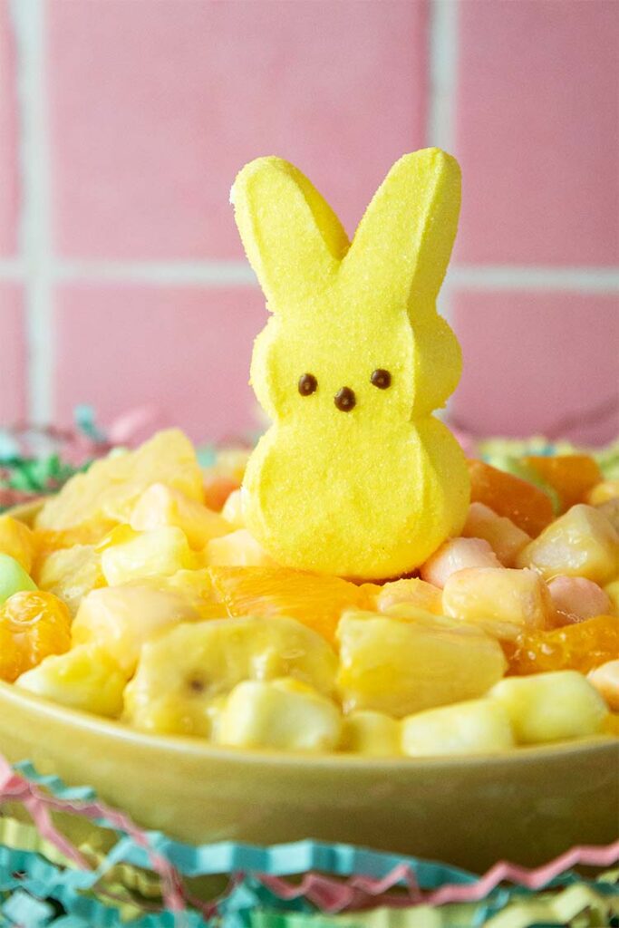 front view of Easter fruit salad in a serving bowl with Easter decor including a yellow Easter peep on top of the salad