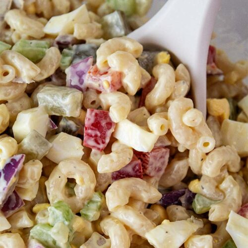 overhead view of macaroni salad ready to serve with a serving spoon removing one serving size