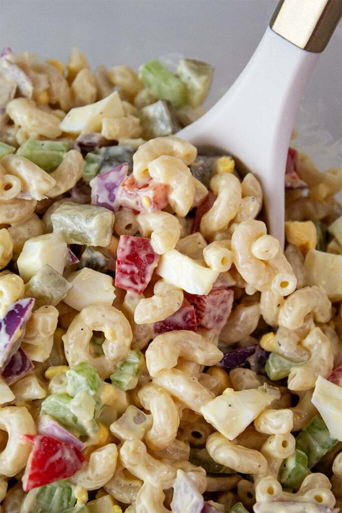 overhead view of macaroni salad ready to serve with a serving spoon removing one serving size