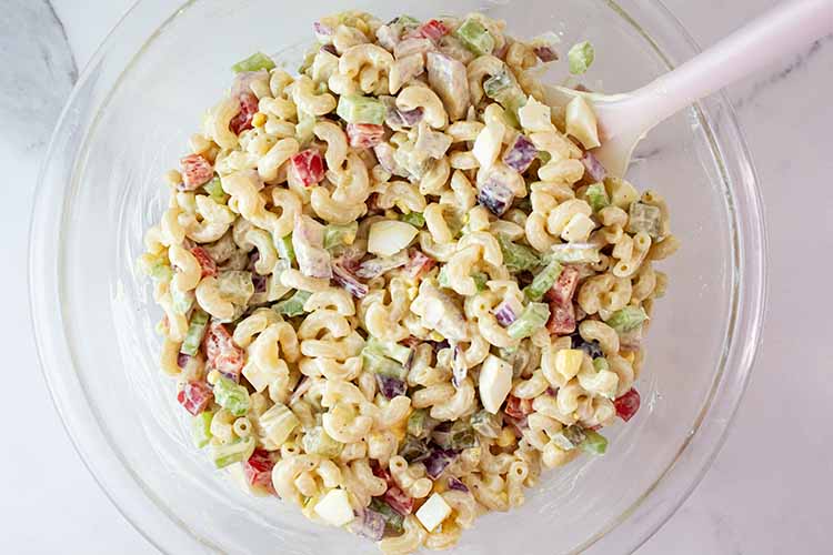 overhead view of fully combined and ready to serve homemade macaroni salad with a serving spoon in it