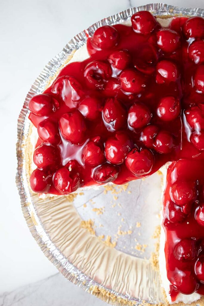 overhead view of no bake cherry cheesecake ready to serve in a pie dish and one serving slice has been removed