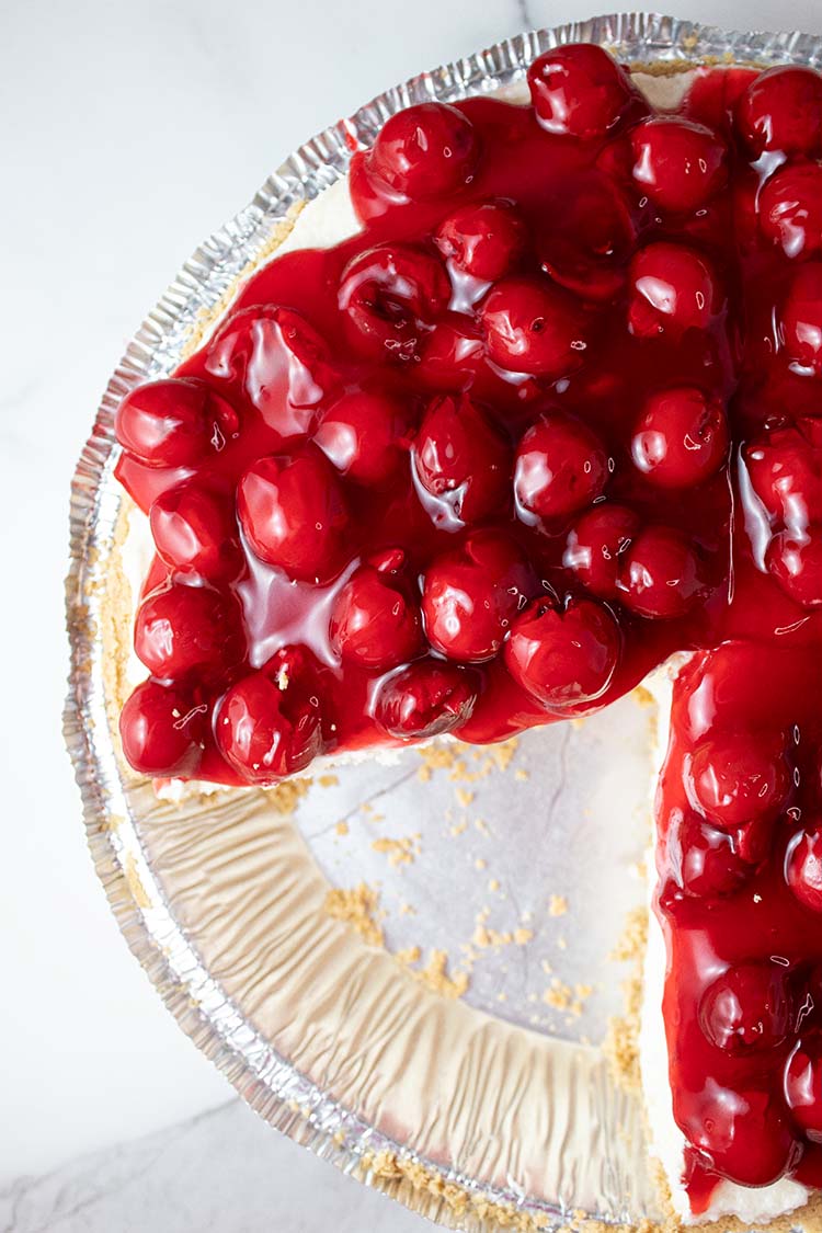overhead view of no bake cherry cheesecake ready to serve in a pie dish and one serving slice has been removed