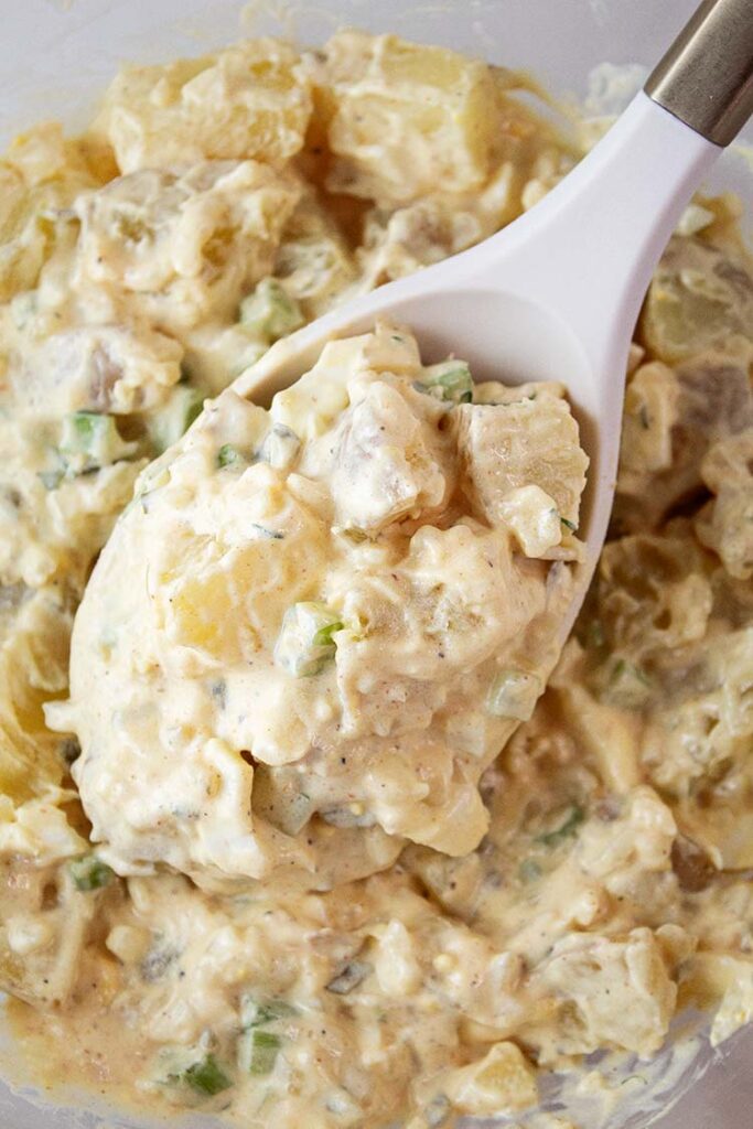 overhead view of potato salad with a serving spoon removing a serving size from a glass serving bowl