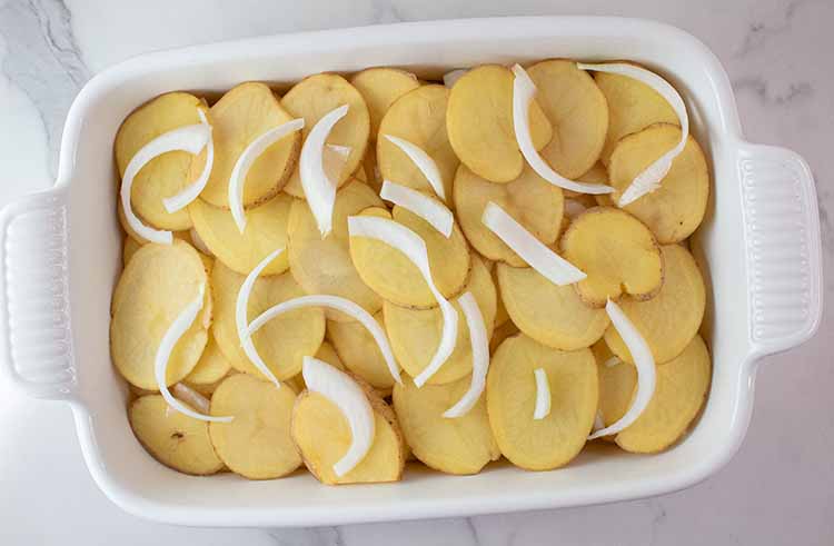 overhead view of layers of scalloped potatoes and onions in a white casserole dish