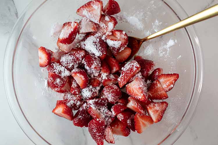 overhead view of sliced strawberries and sugar in a glass mixing bowl ready to be used to assemble each individual shortcake