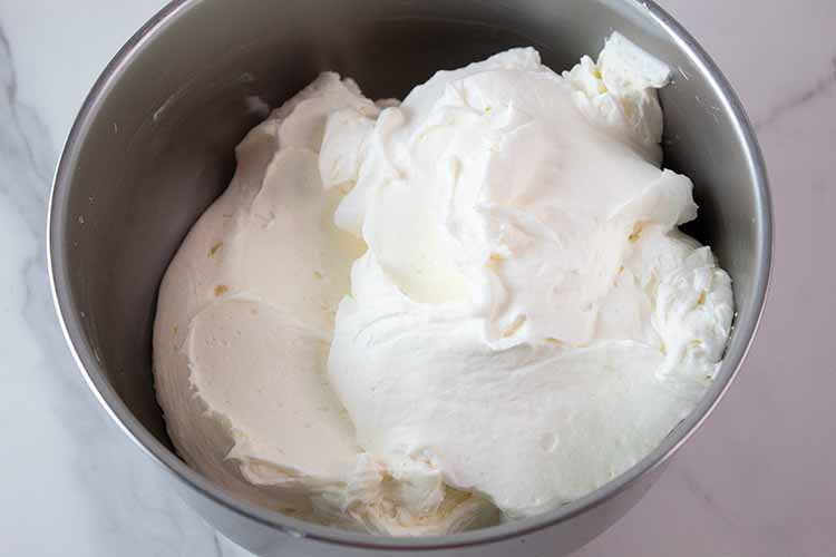 overhead view of steel mixing bowl with whipped cream added to cream cheese mixture and ready to be combined
