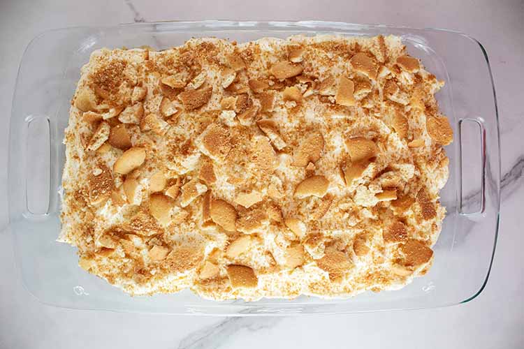 overhead view of banana pudding in a casserole dish and vanilla wafers crumbled onto the top