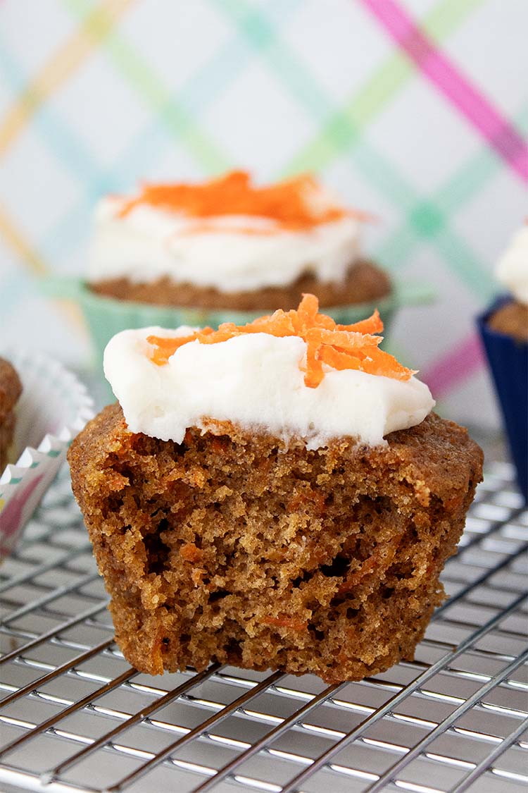 sideview of carrot cake cupcakes with cream cheese frosting and topped with shredded carrots on a cooling rack